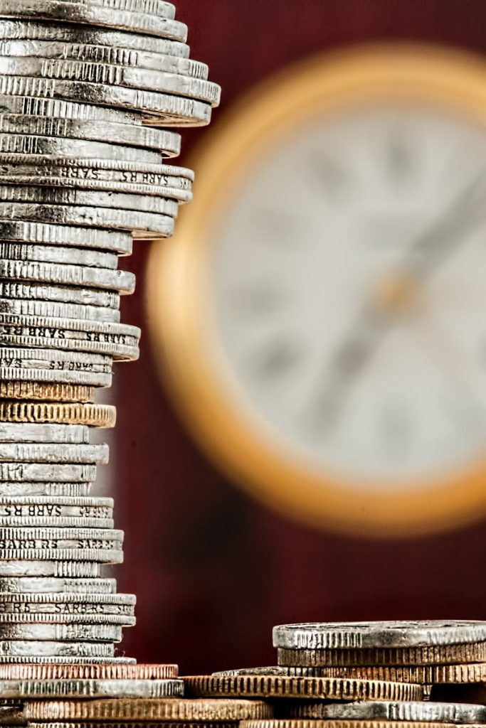 coins-currency-investment-insurance-128867-128867-2 A close-up image of stacked coins with a blurred clock, symbolizing time and money relationship.