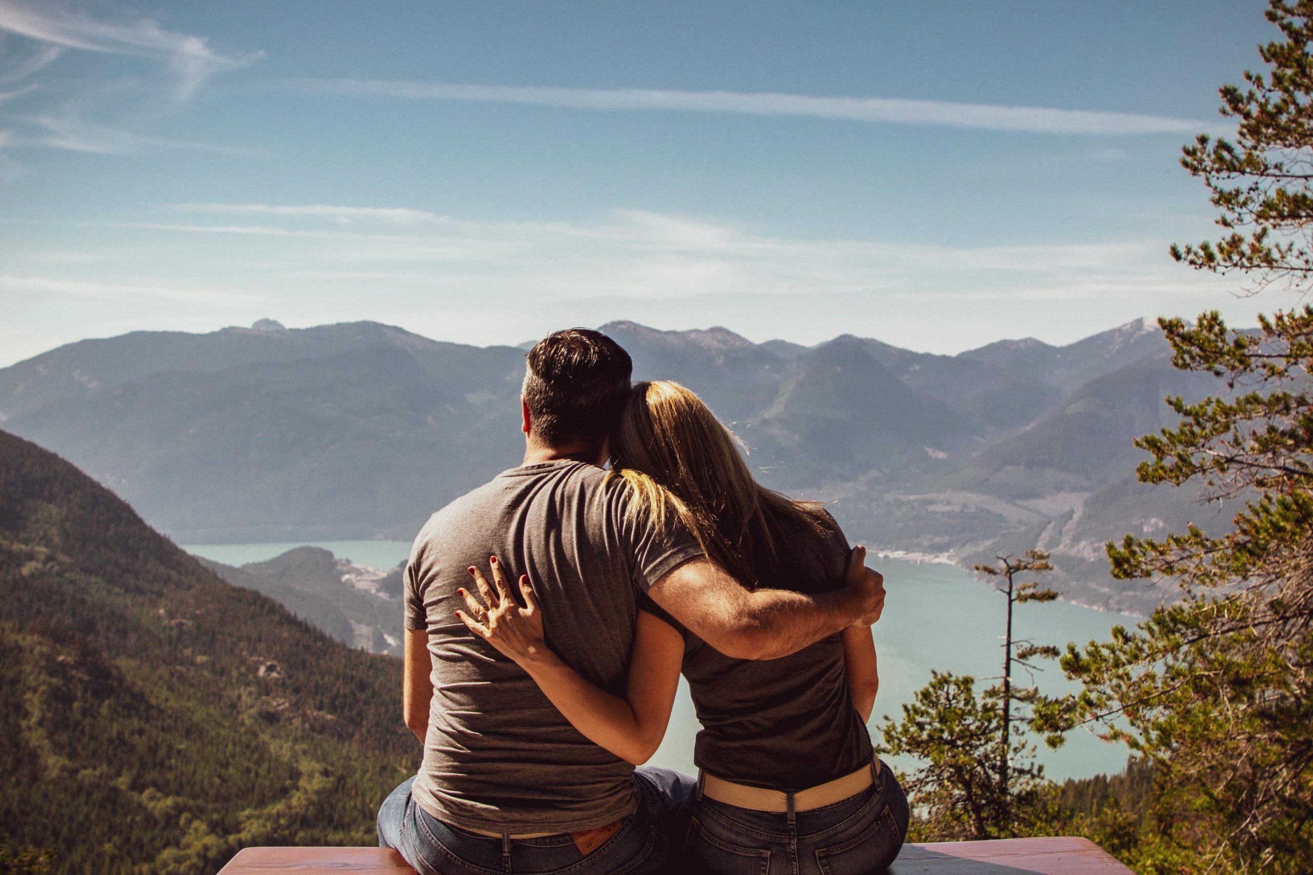 Couple sitting on bench embracing scenic mountain view, embodying romantic nature escape.