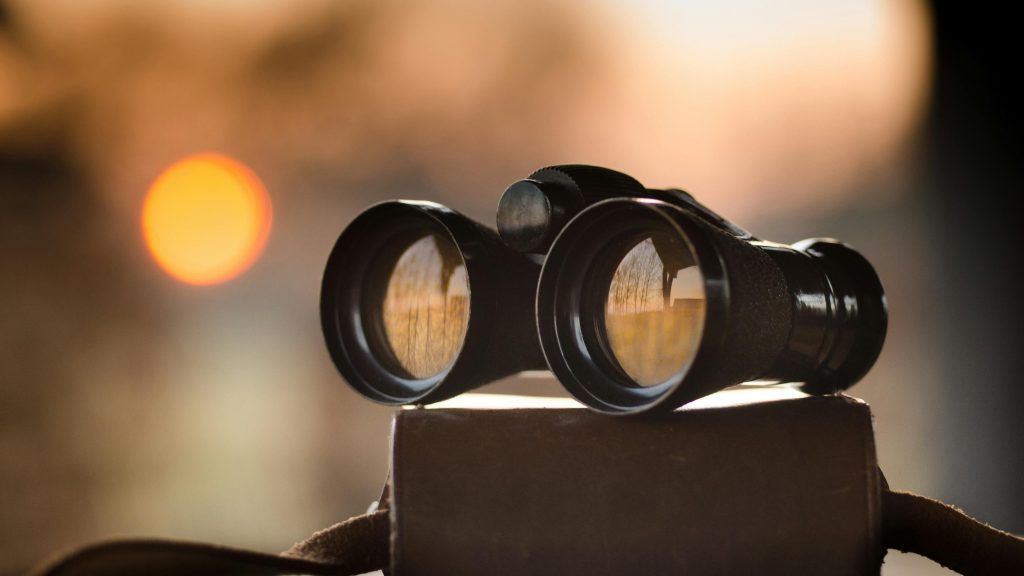Close-up view of binoculars on a surface with sunset reflection in lenses.